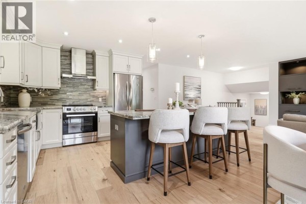 Modern kitchen featuring stainless steel appliances, a grey island with bar stools, and light wood floors. - 2234 Kilbride Street, Burlington
