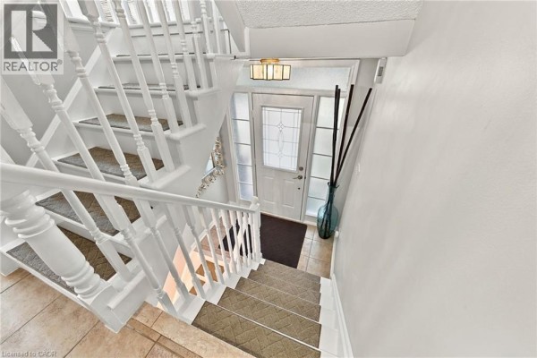 Interior view of a white staircase leading down to a glass-paneled front door with tiled flooring. - 2239 Prescott Place, Burlington