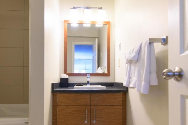 Bathroom vanity with wooden cabinets, dark countertop, mirror, and towels on rack. - 224 - 169 Jozo Weider Boulevard, Blue Mountains