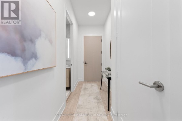 Hallway with light wood floors, a beige door, and abstract art on the wall. - 224 - 858 Dupont Street, Toronto