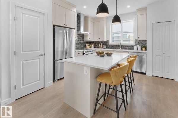 Open concept kitchen with island, pendant lights, and yellow bar stools. - 224 Chappelle Dr Sw, Edmonton