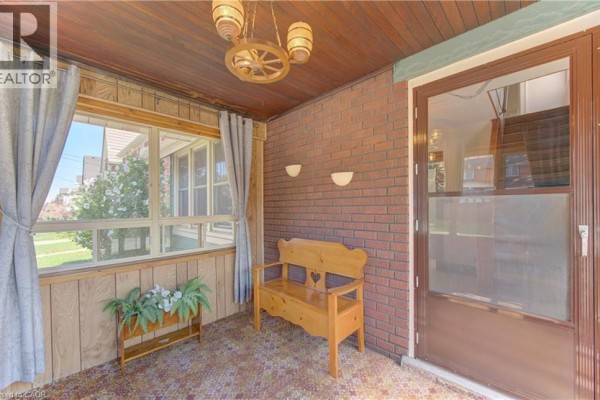 Side view of a red brick house with a screened-in porch and a flowering bush in the front yard. - 224 Weber Street E, Kitchener