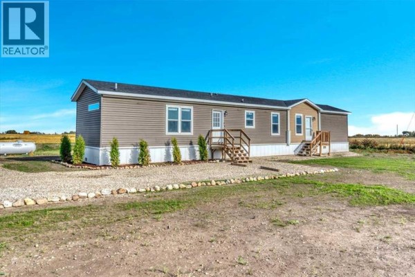 Exterior of a long, tan mobile home with white trim, two sets of stairs, and a gravel driveway. - 224065 Range Rd 262, Rural Wheatland County