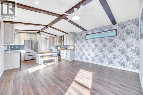 Open concept living area with kitchen, dining table, and decorative wallpaper featuring wood ceiling beams. - 224065 Range Rd 262, Rural Wheatland County