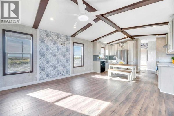Living room and kitchen area with wood-look floors, grey cabinets, stainless steel appliances, and patterned wallpaper. - 224065 Range Rd 262, Rural Wheatland County