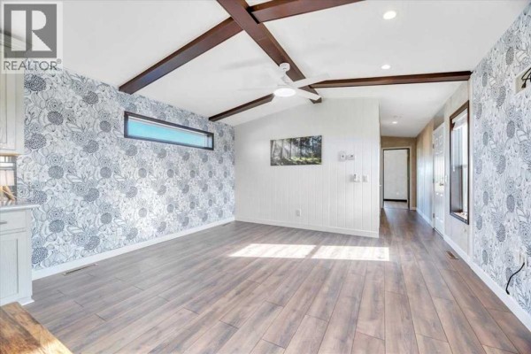 Interior view of the living area, showing patterned wallpaper, wood ceiling beams, and a hallway leading deeper into the home. - 224065 Range Rd 262, Rural Wheatland County