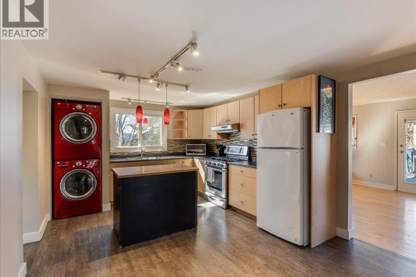 Kitchen with light wood cabinets, black island, and red stacked washer and dryer. - 2243 First Avenue, Rossland