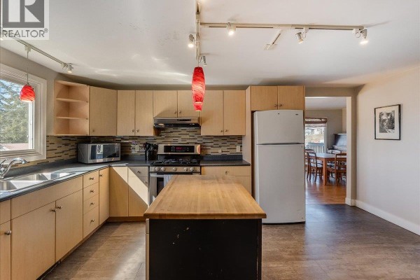 Kitchen with L-shaped counter, wood island, and view into dining area. - 2243 First Avenue, Rossland