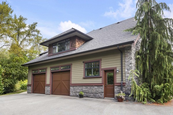 Side view of a garage with three bay doors and a stone base. - 22441 79 Avenue, Langley
