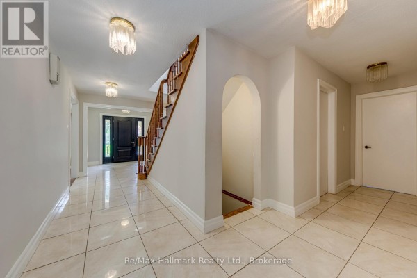 Interior view of the hallway showing a staircase, archway, doors, and tiled flooring with multiple chandeliers. - 2251 Bennington Gate, Oakville