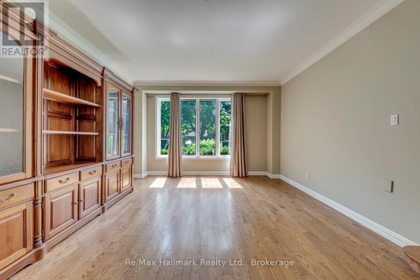 Living room with a large bay window, hardwood floors, and a built-in wooden cabinet with glass doors. - 2251 Bennington Gate, Oakville