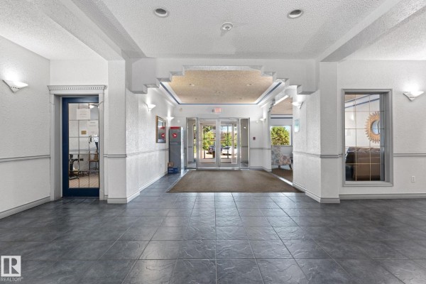 Spacious apartment building lobby with tiled floors, seating areas, and glass double doors. - #225 10511 42 Av Nw, Edmonton