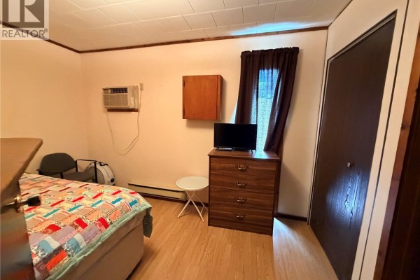 A bedroom with a bed, dresser, air conditioning unit, and a closet with dark curtains. - 225 5th Avenue W, Assiniboia