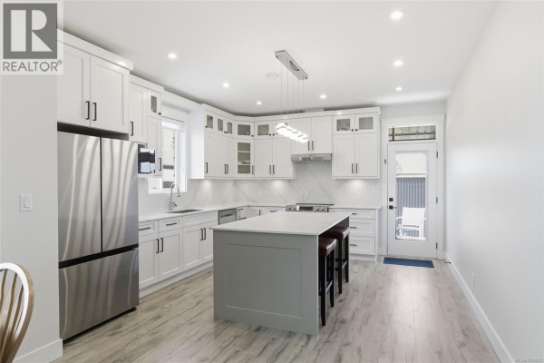 White kitchen with island, bar stools, marble backsplash, and stainless steel appliances. - 225 Dunbar Way, Parksville