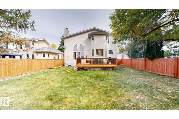 Backyard view of a house with a wooden deck, green grass, and a wooden fence. - 225 Heagle Cr Nw, Edmonton