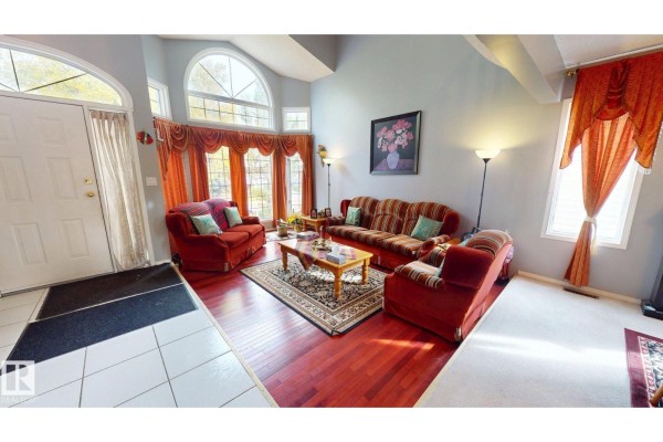 Living room with red sofas, hardwood floors, an arched window with orange drapes, and a patterned rug. - 225 Heagle Cr Nw, Edmonton