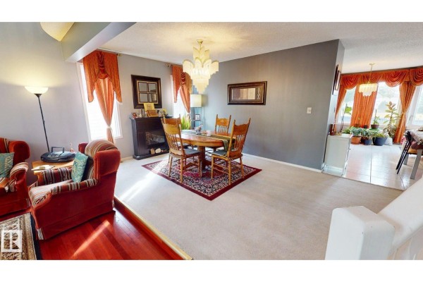Dining room with a wooden table and chairs, patterned rug, fireplace, and orange drapes. - 225 Heagle Cr Nw, Edmonton