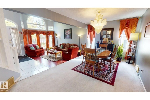 Open-concept living and dining area with red furniture, wood floors, carpet, and large windows. - 225 Heagle Cr Nw, Edmonton