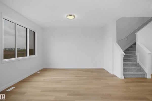 Open-concept kitchen and living area with island, white cabinetry, and light wood flooring - 2250 194a St Nw, Edmonton