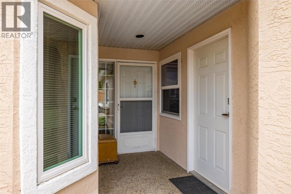 Exterior view of the townhouse with a beige stucco finish, arched garage door, and a paved walkway. - 2250 Louie Drive Unit# 69, Westbank