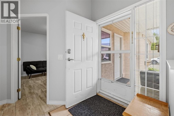Kitchen with white cabinets, dark countertops, a mosaic tile backsplash, and an adjacent living area. - 2250 Louie Drive Unit# 69, Westbank