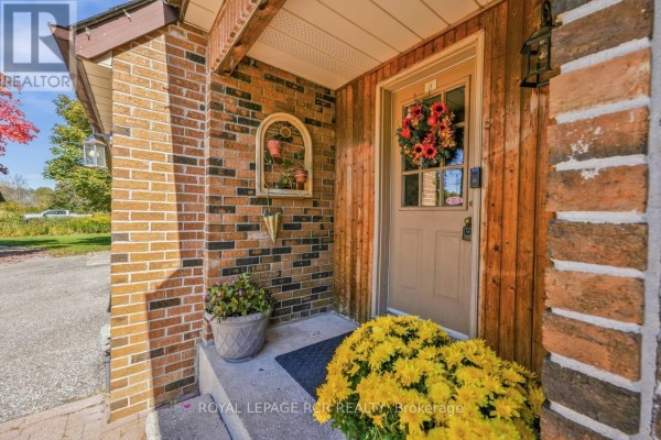 Detail of the covered porch with brick walls, wooden siding, and yellow flowers. - 22541 Kennedy Road, East Gwillimbury