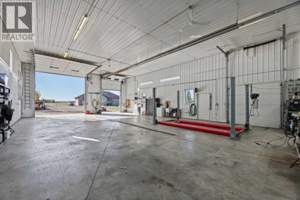 Interior view of a spacious garage with a vehicle lift, multiple garage doors, and concrete floors. - 2256 Township Road 334, Rural Mountain View County