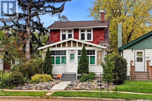Exterior of a two-story house with red siding and a front porch with white railings. - 2257 Elphinstone Street, Regina
