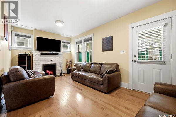 Living room with leather sofas, a white brick fireplace, and a television mounted above. - 2257 Elphinstone Street, Regina