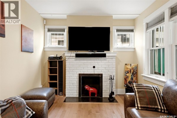 Living room fireplace with a white brick surround, a television, and seating areas. - 2257 Elphinstone Street, Regina