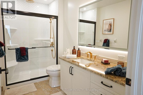 Modern bathroom with a walk-in shower, vanity with granite countertop, and gold-tone fixtures. - 226 - 1050 Canadian Shield Avenue, Ottawa