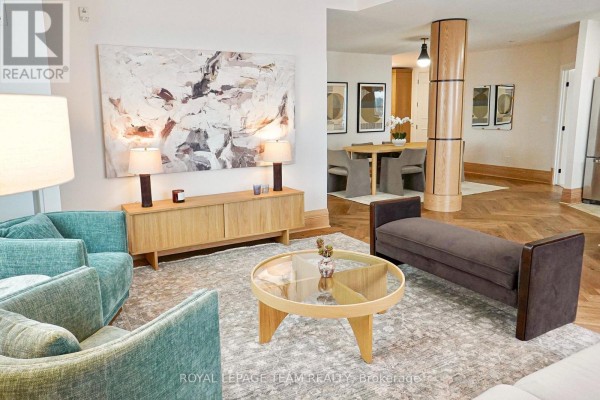 Living room with teal armchairs, glass-top coffee table, and a wooden sideboard, adjacent to a dining area. - 226 - 1050 Canadian Shield Avenue, Ottawa