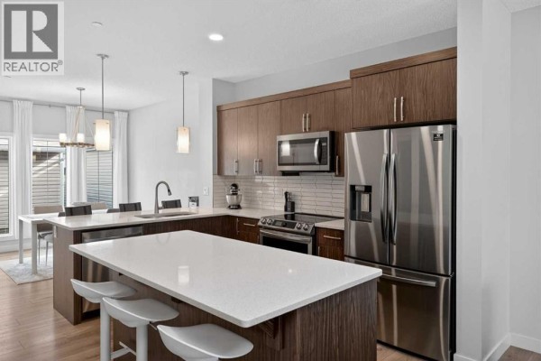 A modern kitchen with dark wood cabinets, a white quartz island, and stainless steel appliances. - 226 148 Avenue Nw, Calgary