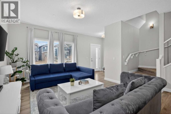 A living room with a blue sectional sofa, grey tufted sofa, and large windows. - 226 148 Avenue Nw, Calgary