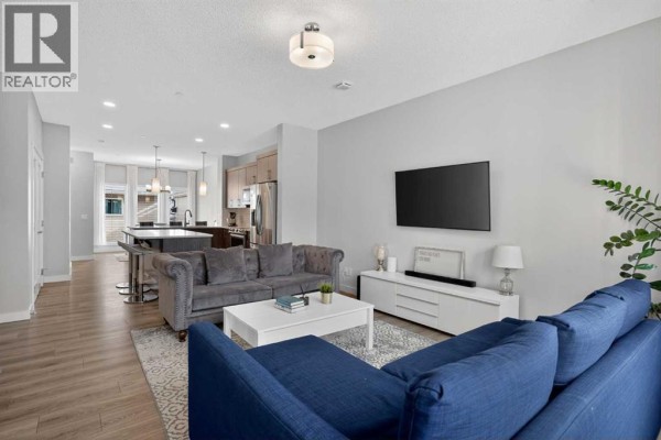 An open-concept living and kitchen area with grey and blue furniture and stainless steel appliances. - 226 148 Avenue Nw, Calgary