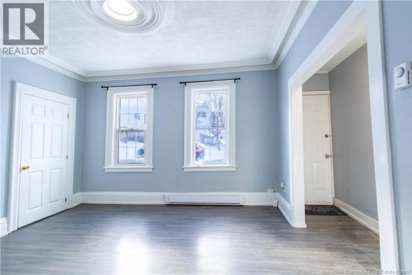 Empty room with grey walls, white trim, dark wood floor, and two windows. - 226-228 Watson Street, Saint John