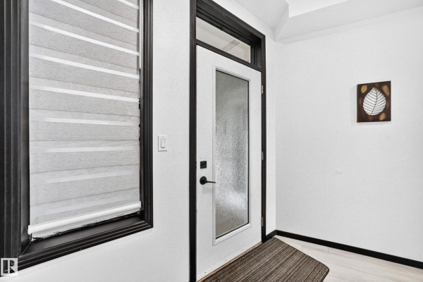 A white entryway with a glass door, textured window blinds, and a leaf-themed wall decoration. - #226 4831 104a St Nw, Edmonton