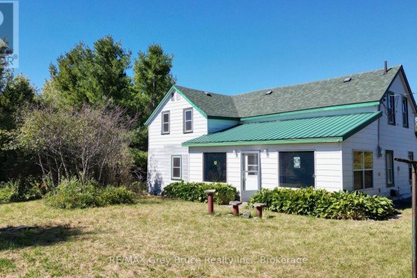 Side view of the white house with a green roof, white siding, and green bushes. - 226 Bartley Drive, Northern Bruce Peninsula