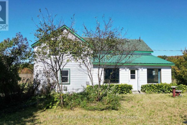 Front view of the white house with white siding, green roof, and surrounding trees. - 226 Bartley Drive, Northern Bruce Peninsula
