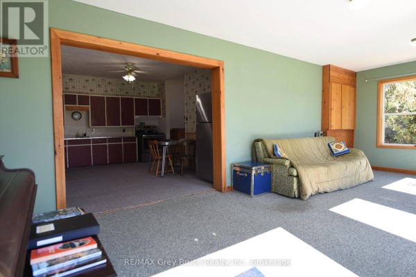 Living room with a green sofa, blue chest, and a doorway opening to the kitchen. - 226 Bartley Drive, Northern Bruce Peninsula
