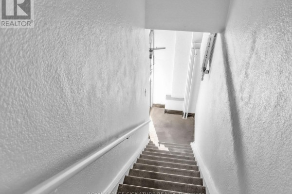 Concrete staircase descends into a dimly lit basement hallway. - 2260 Eglinton Avenue W, Toronto