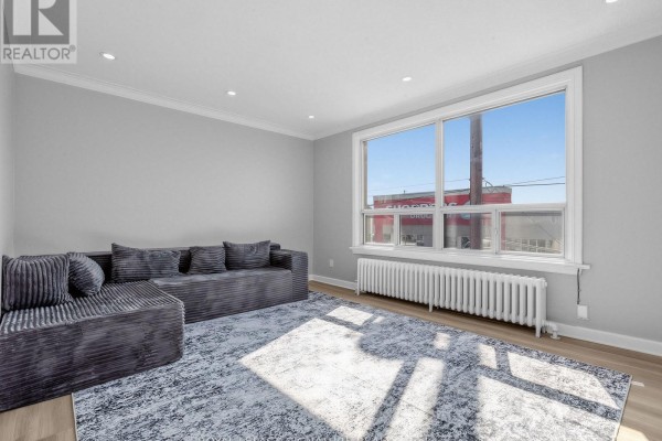 Living room with sectional sofa, patterned rug, and large window with radiator. - 2260 Eglinton Avenue W, Toronto