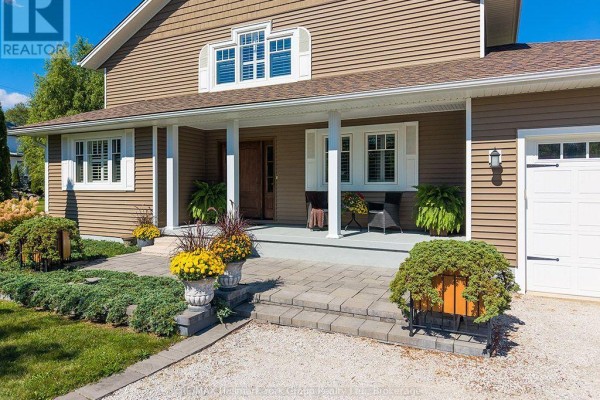 Front entrance of the house with a covered porch, stone steps, and landscaping. - 226083 Centreville Road, Meaford