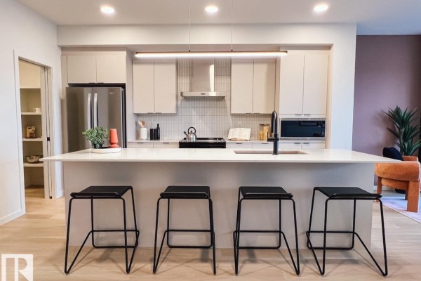 Kitchen island with four black stools facing a white countertop and light gray cabinets. - 22616 85 Av Nw, Edmonton