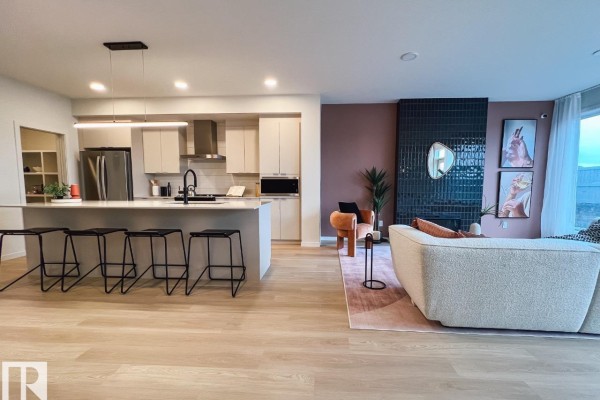 Open concept living area with a kitchen island, sofa, fireplace, and large windows. - 22616 85 Av Nw, Edmonton