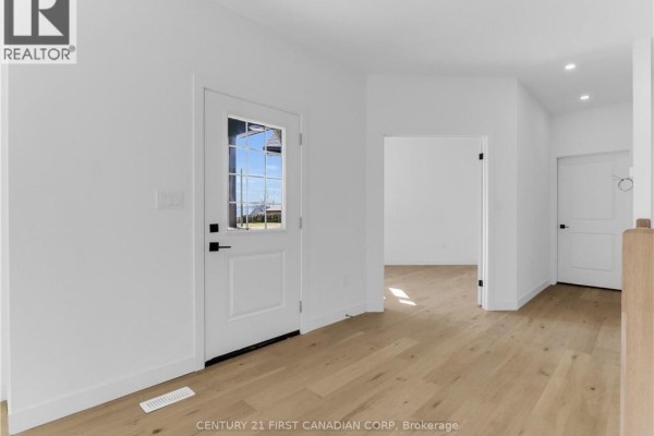 Interior view of a bright foyer with white walls, a glass-paneled front door, and light wood flooring. - 22664 Queens Line, West Elgin