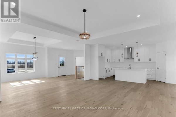 Spacious open-concept living area with white walls, light wood floors, a modern kitchen, and large windows. - 22664 Queens Line, West Elgin