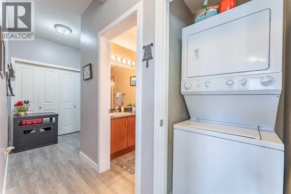 Apartment hallway showing a stacked washer and dryer, a doorway to a bathroom, and double closet doors. - 227, 8 Prestwick Pond Terrace Se, Calgary