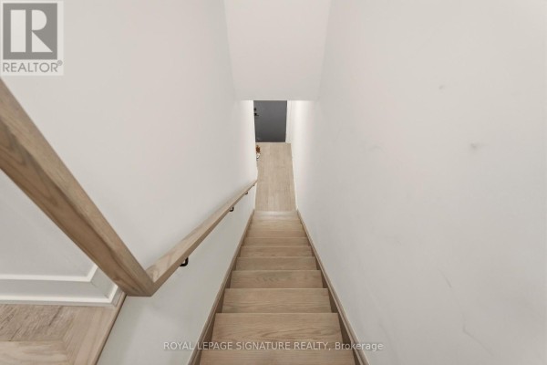 Interior view looking down a modern wooden staircase with white walls and a black railing. - 227 - 1062 Douglas Mccurdy Common, Mississauga