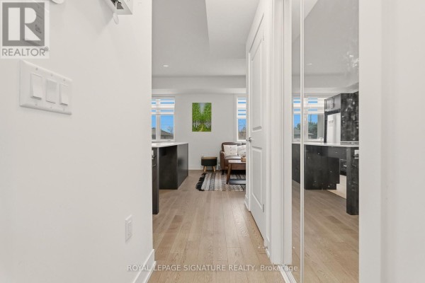 Hallway leading to an open-concept living area with a kitchen island and living room furniture. - 227 - 1062 Douglas Mccurdy Common, Mississauga